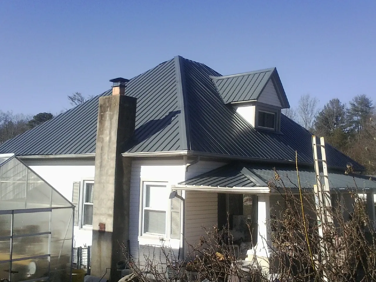 Dark blue standing seam metal roof on a white farmhouse with dormer — Slate & Tile Roof Repair by Roofing Brothers in Avera