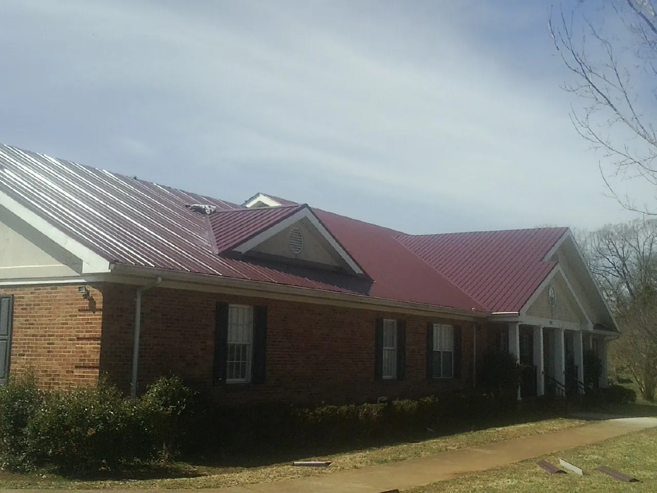 Red metal roof with gabled entries on a long brick building, from a Hail Damage Roof Repair job in Avera