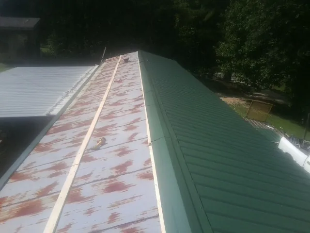 Old rusted panels beside newly installed green metal roofing — Wind Damage Roof Repair by Roofing Brothers in Avera