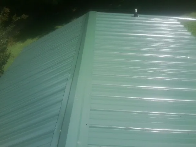 New green metal panels meeting at the ridge of a roof — Flat Roof Repair work by our crew in Avera