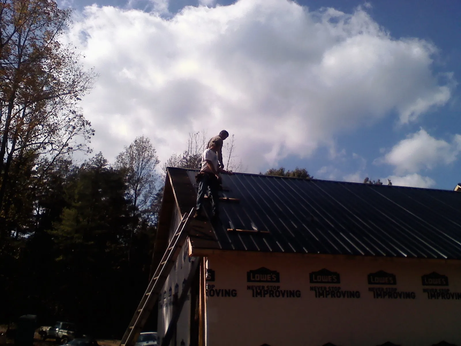 Roofer fastening dark metal panels high against a cloudy sky, from a Roof Inspection job in Avera